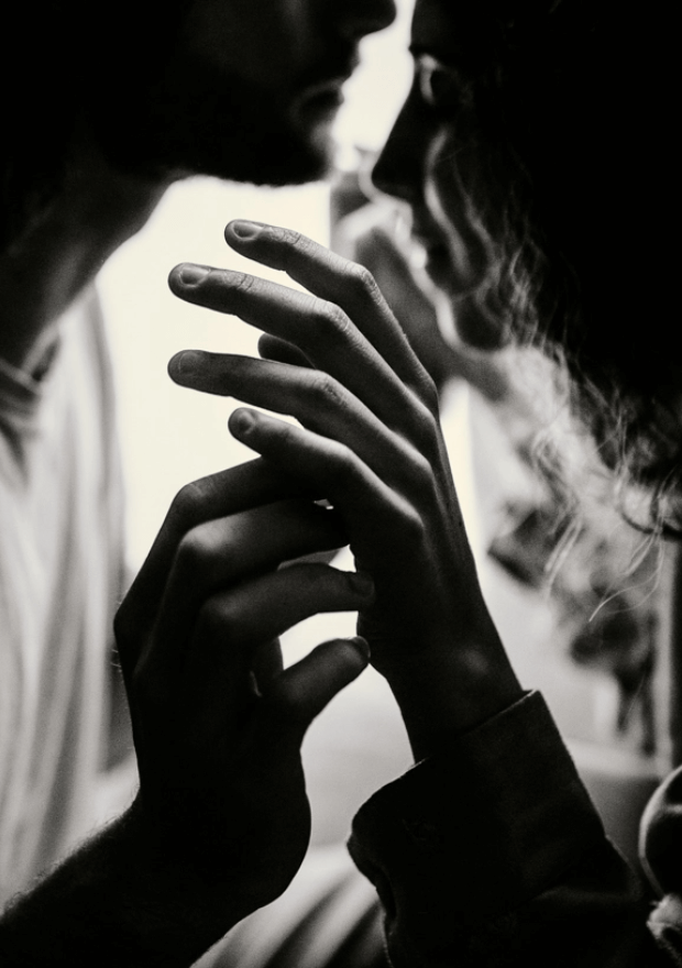 Séance photo de couple intimiste à la maison. Photo en noir et blanc. Photo de leurs mains qui s’entrelacent prise par une photographe de couple