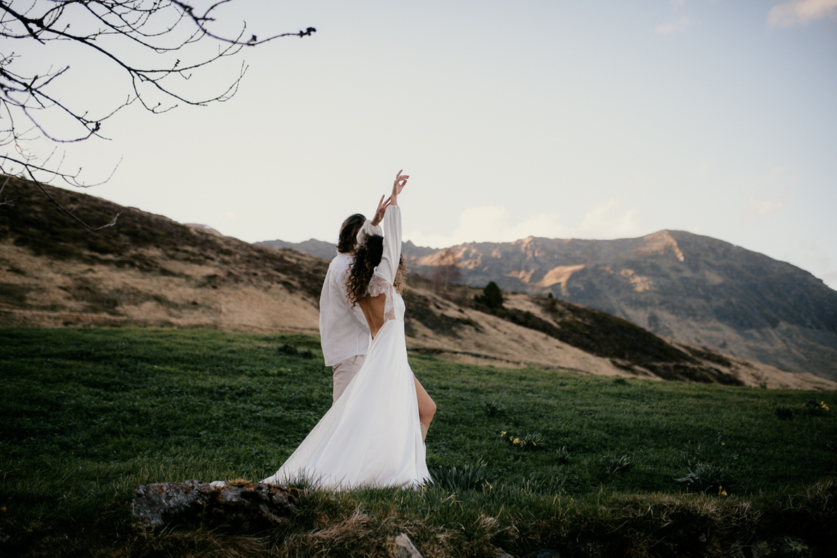 Photo prise par @sophiebacherephotos, plan sur le couple où l'on voit la mariée levé les bras avec arrière plas de la montagne