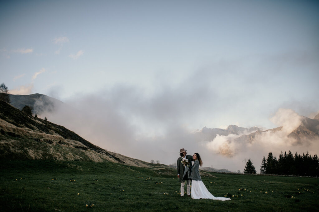 Photo prise par @sophiebacherephotos, plan large où l'on voit l'environnement des montagnes enveloppant les jeunes couples de mariés.