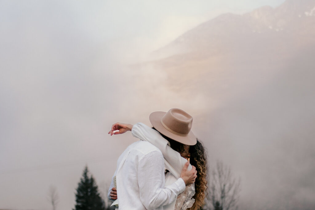 Photo prise par @sophiebacherephotos, plan des mariés qui s'embrasse en arrière plan nuages sur la montagne.