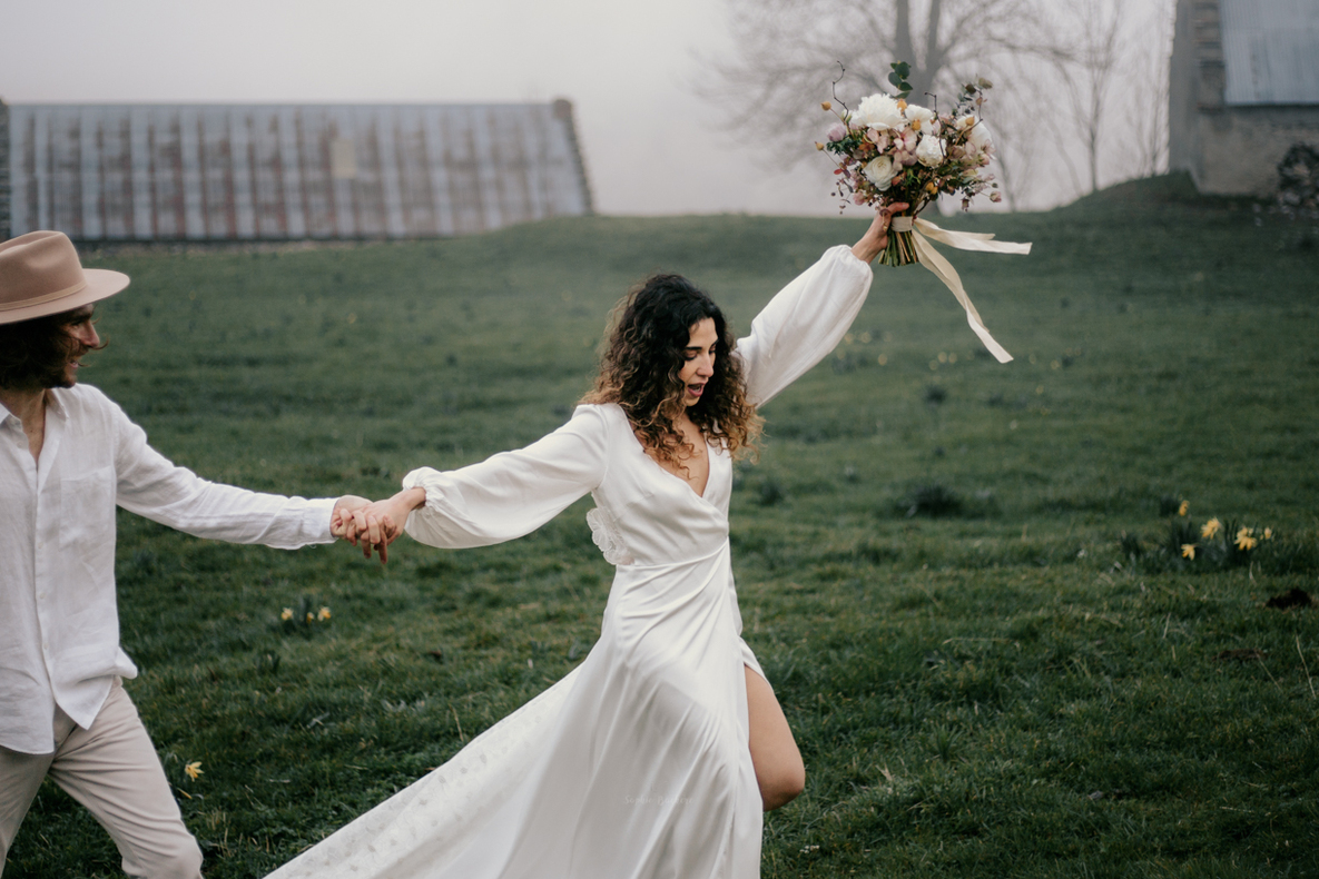 Photo prise par @sophiebacherephotos. Mariée en marchant, brandissant son bouquet de fleurs tout en tenant son mari par la main