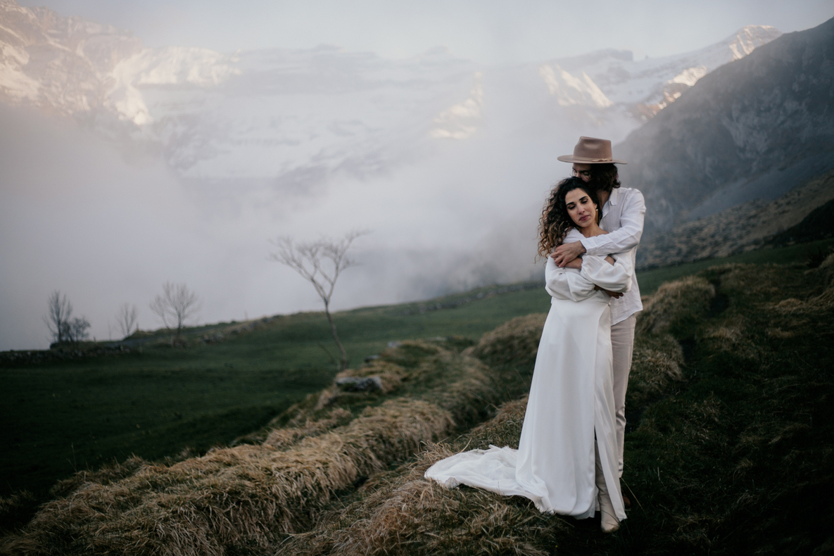 Photo prise par @sophiebacherephotos. Photo des mariées enlacés face caméra avec vu sur les nuages en arrière plan