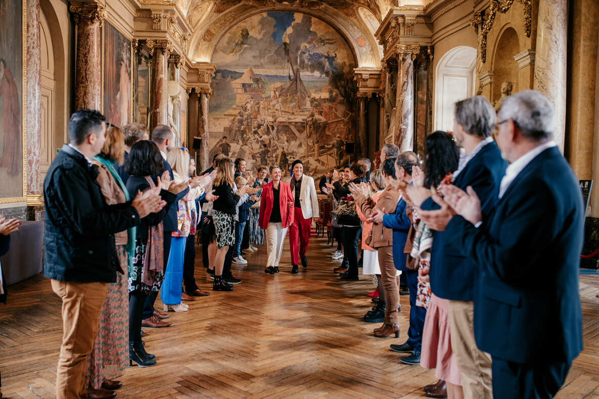 Photo prise par @sophiebacherephotos. La photo montre le couple de futures mariées s'engageant dans l'allée en direction de la sortie de la salle des Illustres