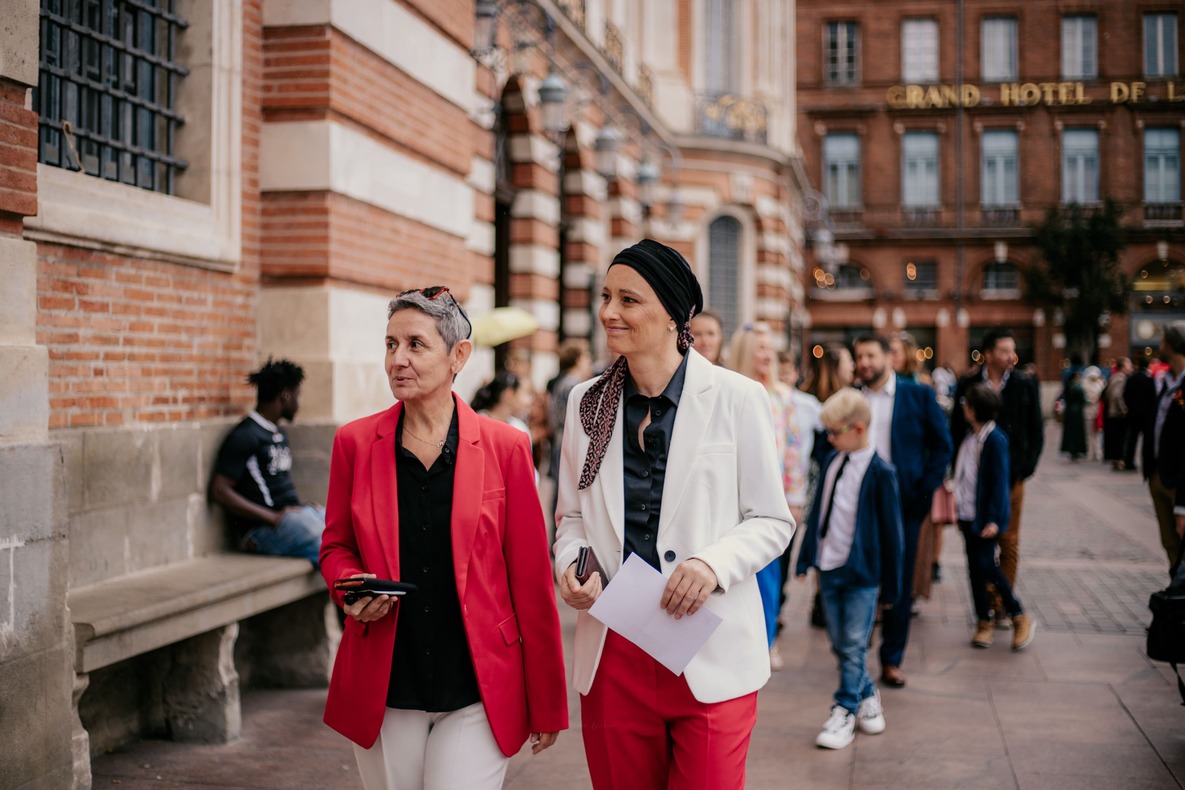 Photo prise par @sophiebacherephotos. La photo montre le couple de futures mariées marchant en direction de la Mairie de Toulouse en Occitanie.