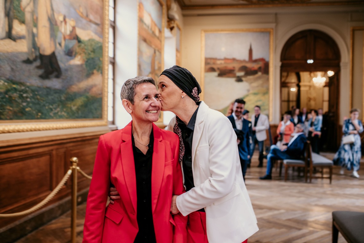 Photo prise par @sophiebacherephotos. La photo montre le couple de futures mariées marchant en direction de la Mairie de Toulouse en Occitanie.