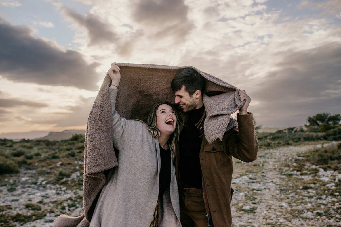 Séance couple par @sophiebacherephotos. La séance photo de couple sur les hauteurs de la clappe près de Narbonne Plage. La photo montre le couple sous une couverture riant aux éclats.