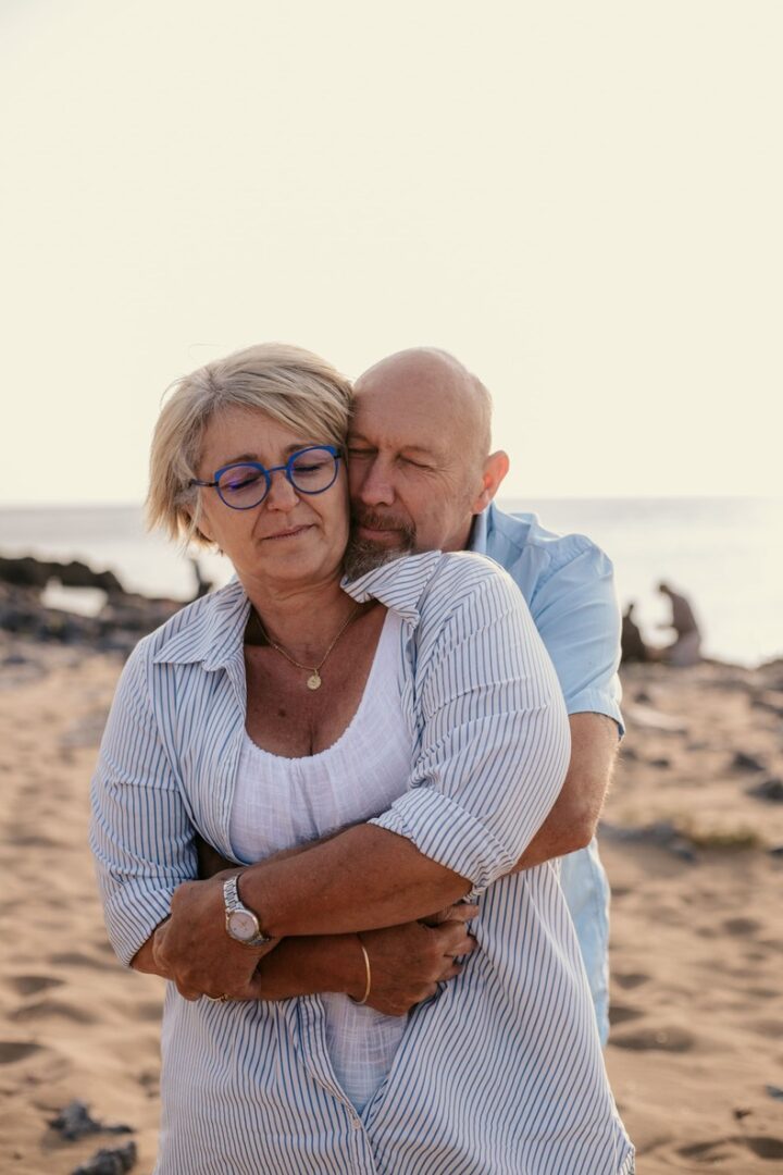 Photo prise par @sophiebacherephotos. Séance photo à la maison, dans la chambre des parents. Les parents ont assis sur leur lit, le bébé est sur les jambes du papa. Les parents regardent avec admiration leur bébé