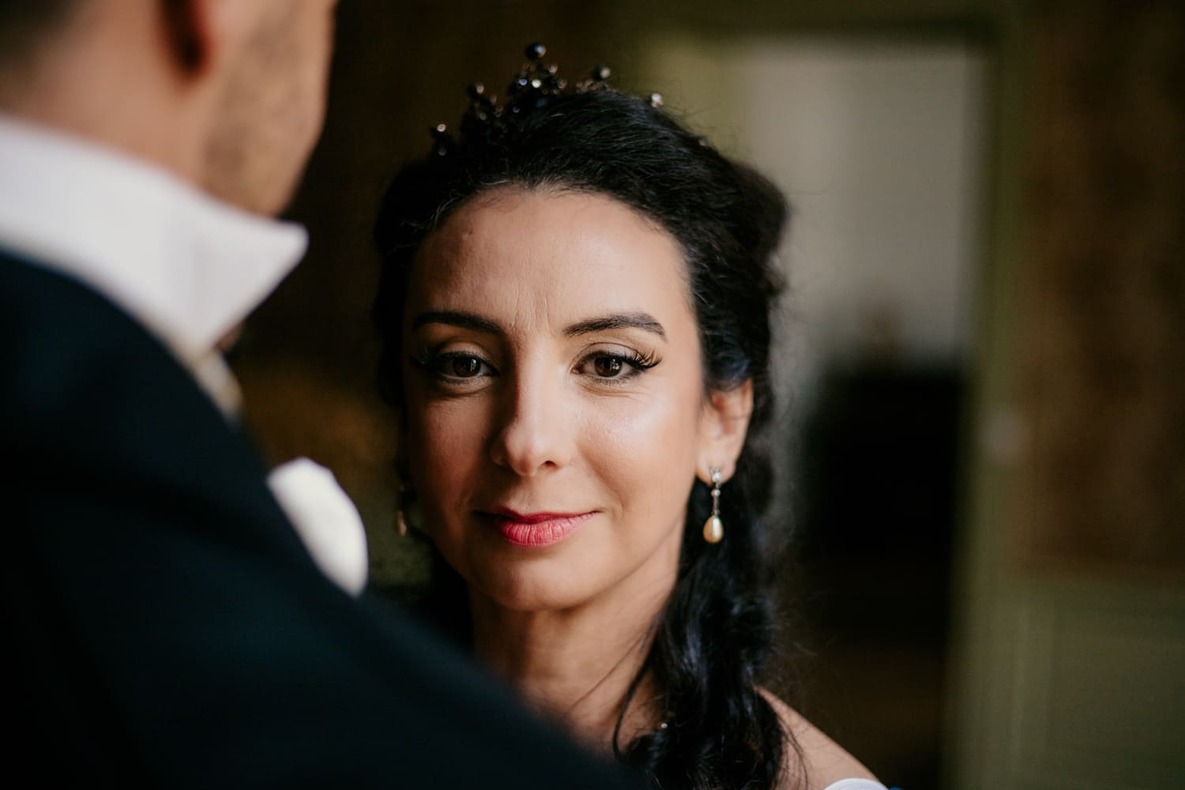 Photo prise par @sophiebacherephotos. La photo montre la mariée regardant l'objectif en souriant alors qu'elle est face à son mari, ils sont dans une salle du Château de Puydaniel