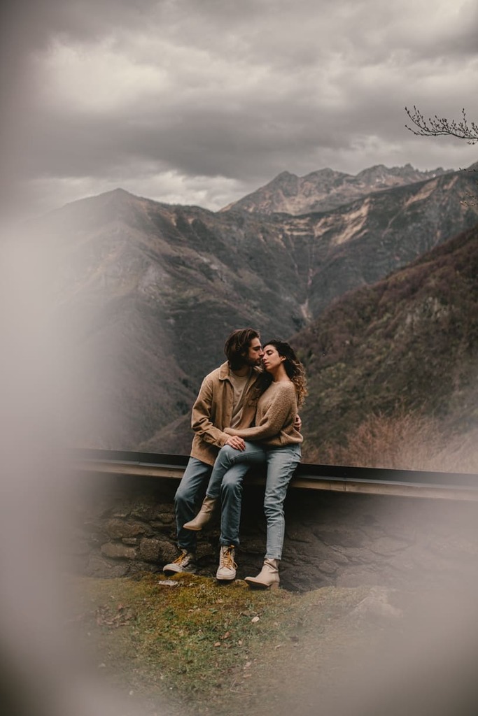 photo prise par @sophiebacherephotos. La photo montre le couple assis sur une rambarde en pierre, en fond les Pyrénées.