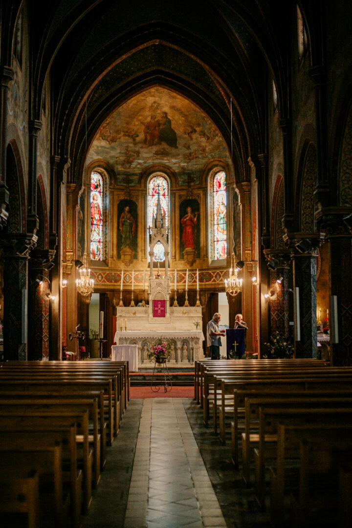 Photo prise par @sophiebacherephotos. Séance photo famille à domicile. La photo montre la maman assise tenant son bébé dans les bras tandis que papa est penché sur son bébé.