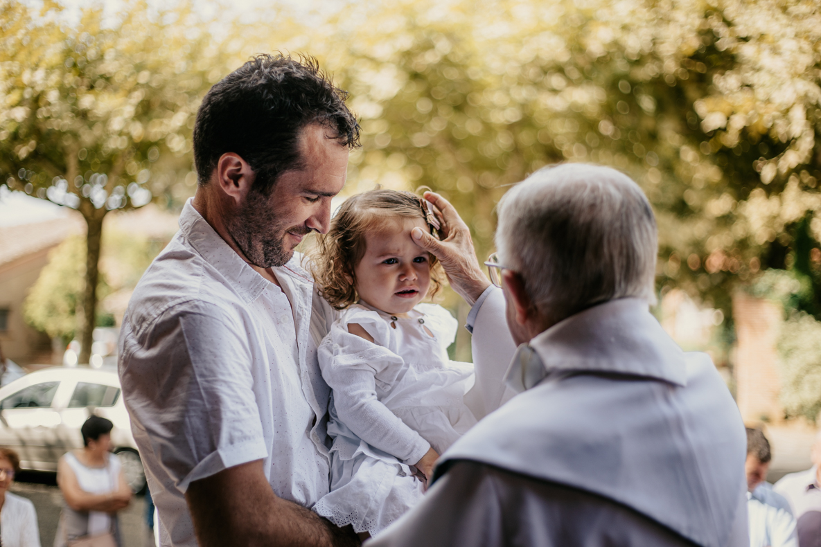 Photo prise par @sophiebacherephotos, le curé bénit l'enfant à l'entrée de l'église